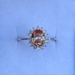 May include: A silver ring with a large oval-shaped orange gemstone surrounded by a halo of smaller white gemstones.