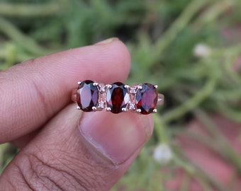 May include: A silver ring with three oval-shaped red gemstones. The ring is set with small white gemstones between the larger red stones.