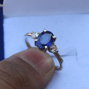 Könnte beinhalten: Ein silberner Ring mit einem blauen ovalen Saphir-Edelstein und drei kleineren weißen Edelsteinen.