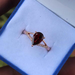May include: A pear-shaped garnet ring set in rose gold with a delicate diamond band.