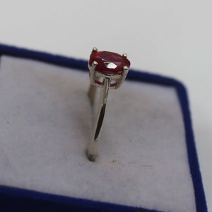Puede incluir: Un anillo de plata con una vibrante gema de rub&iacute; de corte ovalado. El rub&iacute; es de color rojo intenso y est&aacute; engastado en un engaste cl&aacute;sico de cuatro garras. El anillo se exhibe en una caja de terciopelo azul.