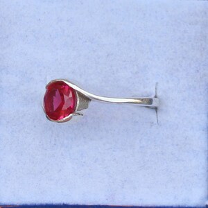 May include: A silver ring featuring a vibrant red oval gemstone. The gemstone is the focal point, set in a sleek, minimalist design. The ring is displayed against a light blue background.