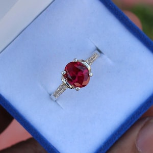 May include: A silver ring with a large oval-shaped red gemstone surrounded by smaller clear gemstones.
