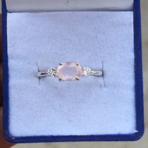 May include: A silver ring with a pink oval gemstone and two smaller round gemstones on either side.