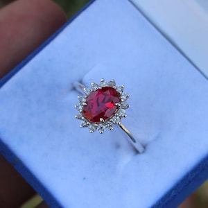 May include: A silver ring with a large oval red gemstone surrounded by smaller white gemstones.