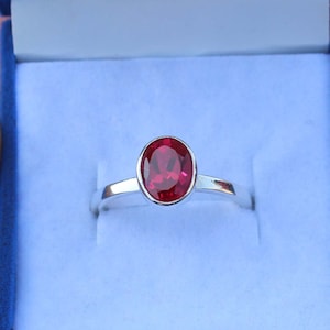 May include: A silver ring with a bright red oval gemstone.