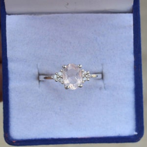 Puede incluir: Un anillo de plata con una gran piedra rosa ovalada rodeada de piedras pequeñas transparentes.