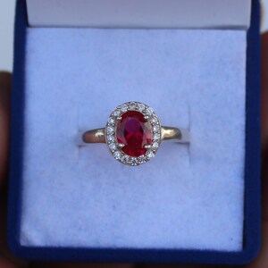 Può includere: Un anello d'argento con un grande rubino rosso ovale circondato da un'aureola di piccoli diamanti bianchi.