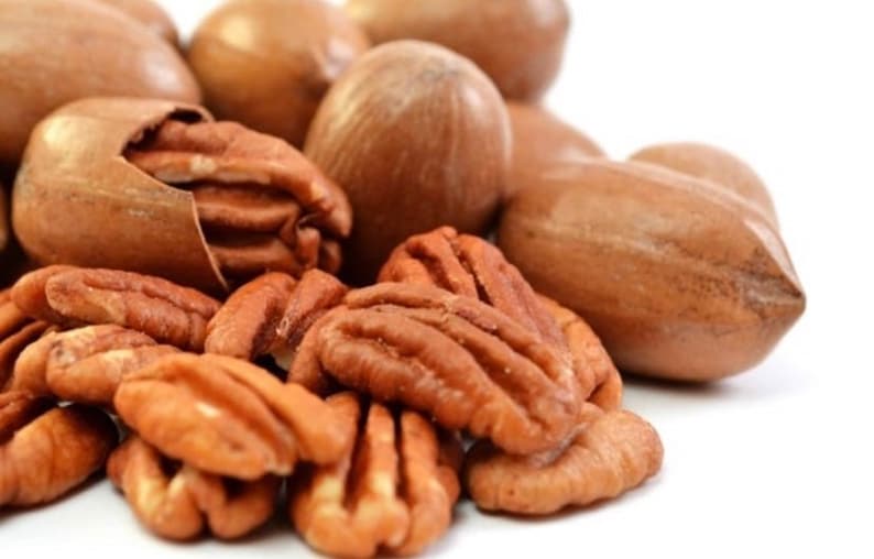Puede incluir: Primer plano de nueces de pacana, algunas todav&iacute;a en sus c&aacute;scaras y otras descascaradas. Las pacanas son de color marr&oacute;n claro y tienen una textura ligeramente rugosa.