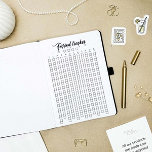 May include: A white period tracker with black grid squares and the text "Period Tracker" written in black cursive. The tracker is divided into months, with the abbreviations "J F M A M J J A S O N D" written across the top.