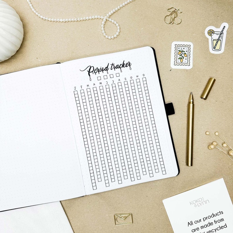 May include: A white period tracker with black grid squares and the text "Period Tracker" written in black cursive. The tracker is divided into months, with the abbreviations "J F M A M J J A S O N D" written across the top.