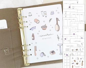 May include: A brown leather bound planner with gold rings. The planner has a white page with a hand-drawn illustration of bath and beauty products. The page is labeled "November" with the days of the week abbreviated. The planner also includes a set of printable stickers with bath and beauty product illustrations.