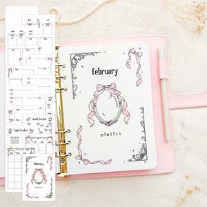 Peut inclure: Un agenda rose avec des anneaux dorés, ouvert sur une page avec le mot "février" et des nœuds décoratifs. Plusieurs inserts de planification avec des calendriers et des trackers sont visibles. Un stylo repose dans la tranche de l'agenda.