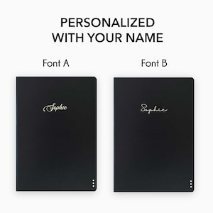 May include: Two black leather notebooks with gold lettering. The notebooks are personalized with the name "Sophie" in two different fonts. Font A is a cursive script font. Font B is a more modern, sans-serif font.