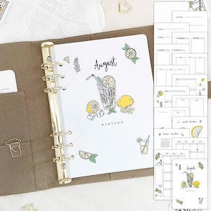 May include: A white planner with gold rings and a clear plastic cover. The planner has a monthly calendar page for August with a lemon-themed illustration and the text "August". The planner also includes several other pages with different layouts for planning and tracking.