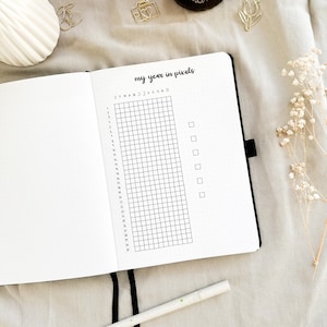 以下が含まれることがあります： 「my year in pixels」というタイトルの白黒のプランナーページ。ページは、月の曜日と年を表す31行12列のグリッドに分割されています。ページの右側には、空のボックスが5つあります。