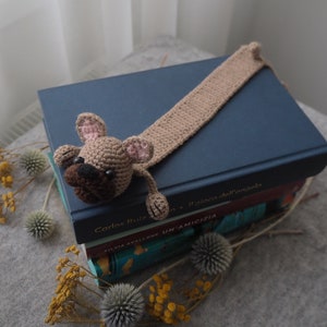 May include: A crocheted brown and pink dog bookmark with a long tail, sitting on top of a stack of books. The top book is blue and has the text "Carlos Ruiz Zafon" on the spine.