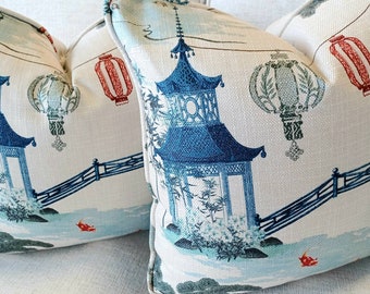 May include: Two white throw pillows with a blue and green Asian-inspired design. The pillows feature a pagoda, lanterns, and a bridge.