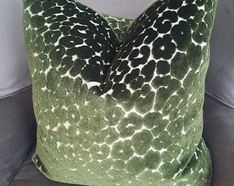 May include: A green velvet throw pillow with a white abstract pattern. The pillow is sitting on a gray armchair.
