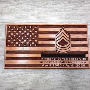 Puede incluir: Una placa de madera con un diseño de bandera estadounidense, una insignia de rango militar y el texto "En honor a 20 años de servicio en la Reserva del Ejército de los Estados Unidos Abril 2005 - Abril 2025".