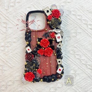 May include: A red, black, and gold phone case with a playing card theme. The case is decorated with roses, playing cards, and a small gun charm. The case is made of a hard plastic material and has a clear back.
