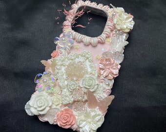May include: A pink phone case decorated with various embellishments. It includes white and pink flowers, iridescent butterflies, and pearl accents. The case has a textured, layered design with a camera cutout.