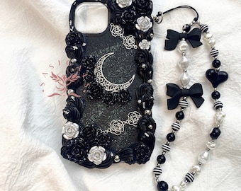 May include: Black phone case with a crescent moon and black roses design. The case has a black and white beaded phone strap with a black heart charm.