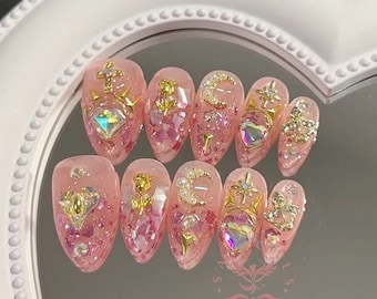 May include: Pink and gold press-on nails with various embellishments, including hearts, stars, moons, and flowers.
