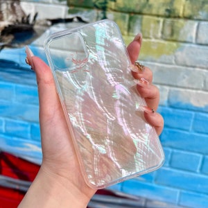 Puede incluir: Una funda de teléfono transparente con un acabado nacarado iridiscente. La funda tiene un pequeño logotipo en la parte posterior que dice "SPIRIT".