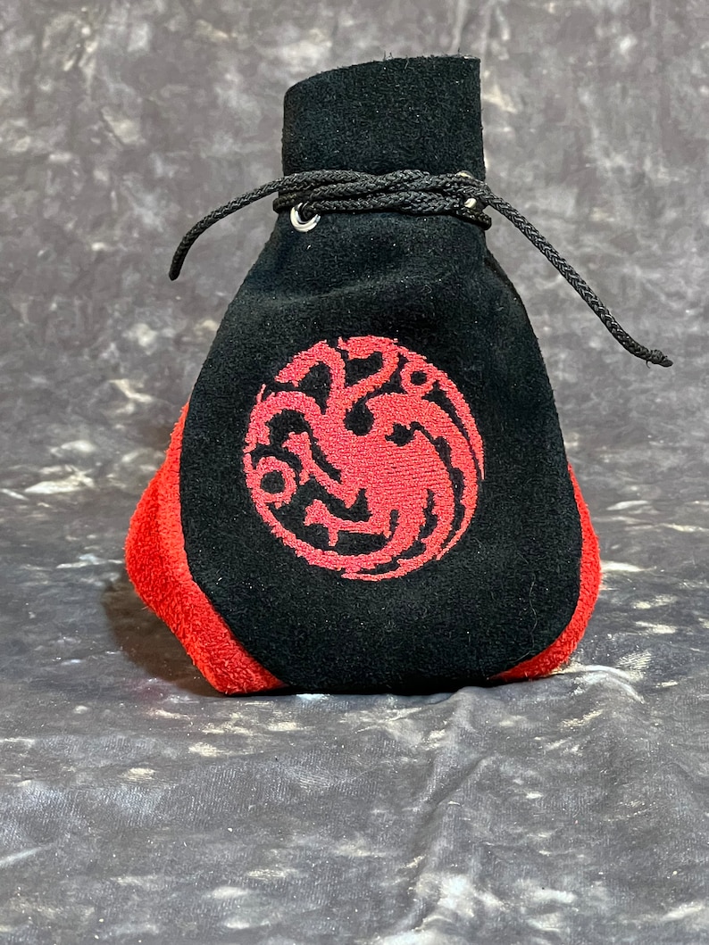 May include: Black suede drawstring bag with a red embroidered dragon design. The bag has a red lining and a silver metal drawstring closure.