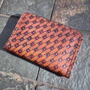 May include: A brown leather wallet with a red and brown geometric pattern. The wallet has a stitched edge and a flap closure.