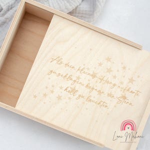 Könnte beinhalten: Eine Holzkiste mit einem Schiebedeckel. Der Deckel ist mit dem Text "Als dein kleines Herz aufhörte zu schlagen begann ein Stern hell zu leuchten" und einer Streuung von Sternen graviert. Die Box ist von Loni Mahoni hergestellt.