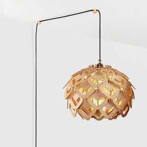 May include: A wooden pendant light fixture with a geometric design hangs from a black cord. The light is suspended from the ceiling with a black cord and a gold-colored ceiling mount.