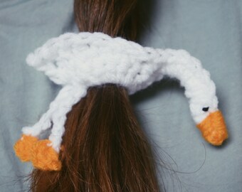 May include: White crocheted swan hair tie with orange beak and feet.
