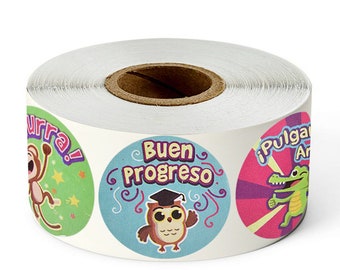 May include: Roll of colorful round stickers with various designs and Spanish phrases. The stickers feature a monkey, an owl wearing a graduation cap, and an alligator. The phrases on the stickers are "¡Hurra!" "Buen Progreso" and "¡Pulgar Arriba!"