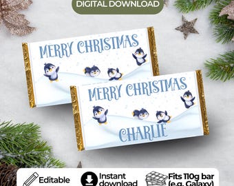 May include: Two chocolate bar wrappers with gold foil edges, featuring a winter scene with penguins and the text "MERRY CHRISTMAS" in blue. One wrapper has the name "CHARLIE". The wrappers are designed to fit a 110g bar.