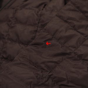 May include: Close-up of a dark brown quilted jacket. The jacket has a diamond pattern and appears to be made of a lightweight material. The fabric has a slight sheen, suggesting a possible water-resistant finish. The overall aesthetic is simple and functional.