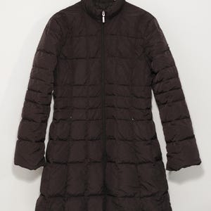 May include: A dark brown, quilted puffer coat with a full-length design. The coat features a stand-up collar, a full-length zipper, and long sleeves. The coat is hanging on a wooden hanger against a white background.