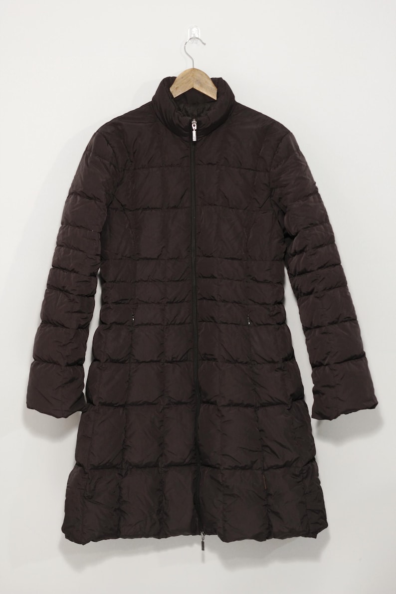 May include: A dark brown, quilted puffer coat with a full-length design. The coat features a stand-up collar, a full-length zipper, and long sleeves. The coat is hanging on a wooden hanger against a white background.