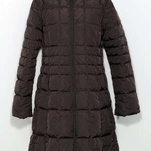 May include: A dark brown, quilted, long coat with a high collar and a full-length zipper. The coat has long sleeves and a slightly flared bottom hem. The coat is displayed on a white background.