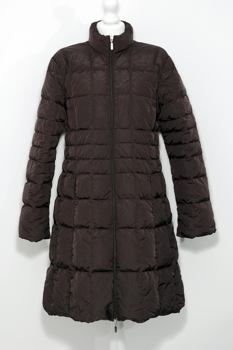 May include: A dark brown, quilted, long coat with a high collar and a full-length zipper. The coat has long sleeves and a slightly flared bottom hem. The coat is displayed on a white background.