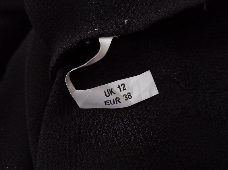 Może przedstawiać: Biała metka z czarnym tekstem wskazująca rozmiar odzieży: UK 12 EUR 38.