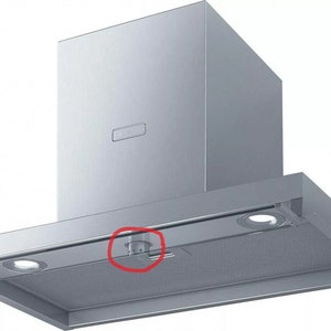 Könnte beinhalten: Eine Dunstabzugshaube aus Edelstahl mit einem schwarzen Drehknopf und zwei Lichtern. Die Haube hat eine rechteckige Form und eine silberne Oberfläche.