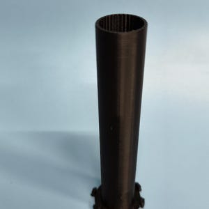 May include: A black plastic tube with a textured surface and a circular base with a scalloped edge.