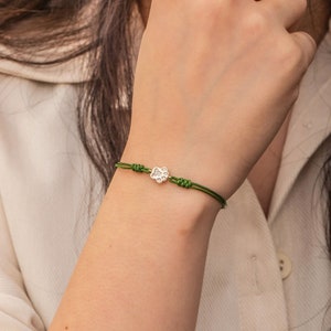 May include: A green string bracelet with a small silver paw print charm. The charm is decorated with small clear crystals.
