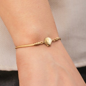 May include: A gold seashell charm bracelet with a delicate gold chain. The bracelet is adjustable and has a simple design.