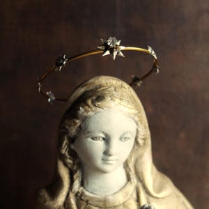 May include: A white plaster statue of a woman wearing a gold halo with star-shaped accents. The statue is wearing a white robe and has a soft, gentle expression.