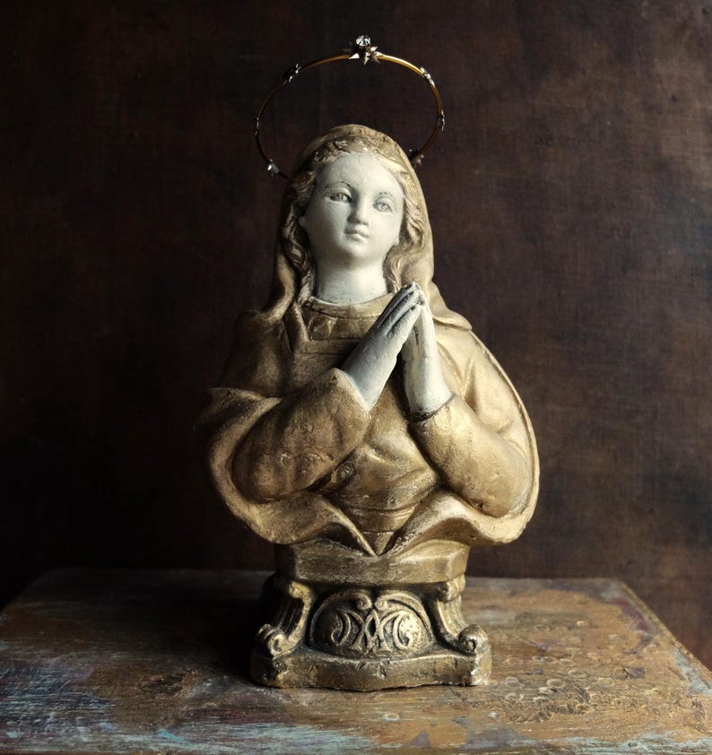 May include: A gold-painted plaster bust of a woman with a halo, wearing a robe and praying with her hands clasped together.
