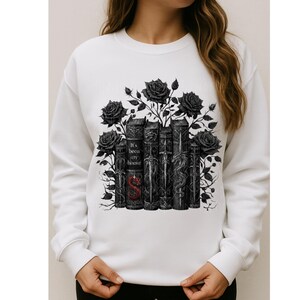 May include: White sweatshirt featuring a graphic of black roses and stylized books. The books have intricate designs and the text "It's been my honor" with a red "S" on one. A stylish and unique design.