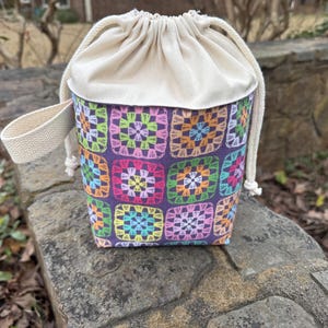 May include: A small, drawstring bag with a white cotton lining and a colorful crocheted pattern. The bag has a single strap for carrying.
